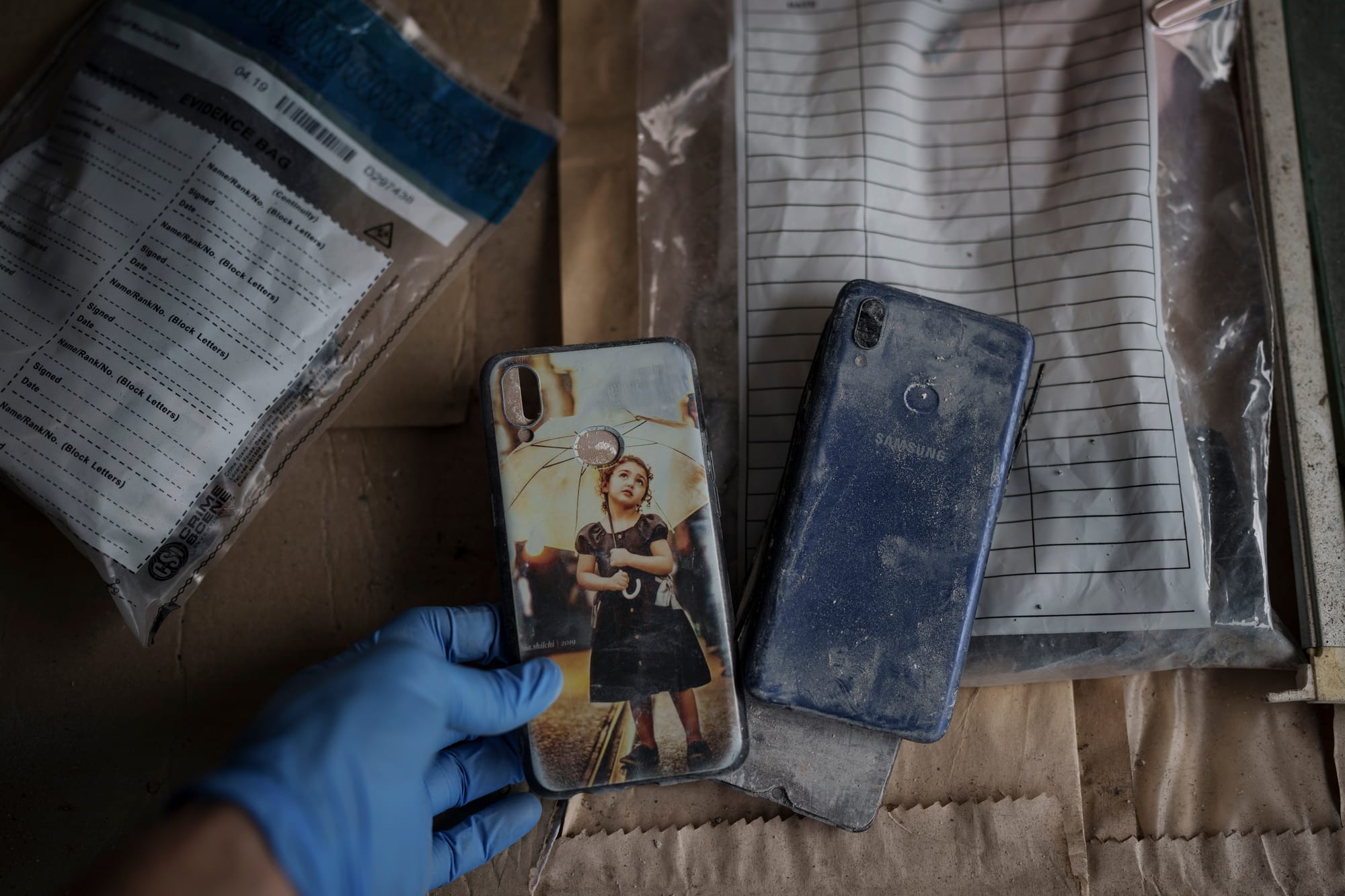 A gloved hand lifts the phone cover off of a dirty Samsung phone. The phone cover features an image of a little girl holding an umbrella.