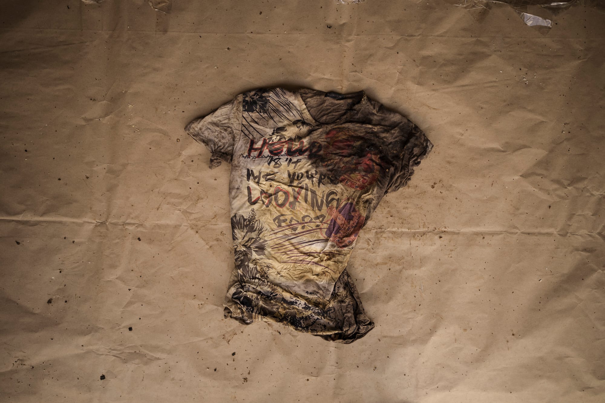 A muddy wrinkled shirt is laid out on a brown piece of paper. Text on the shirt reads “Hello is it me you’re looking for”