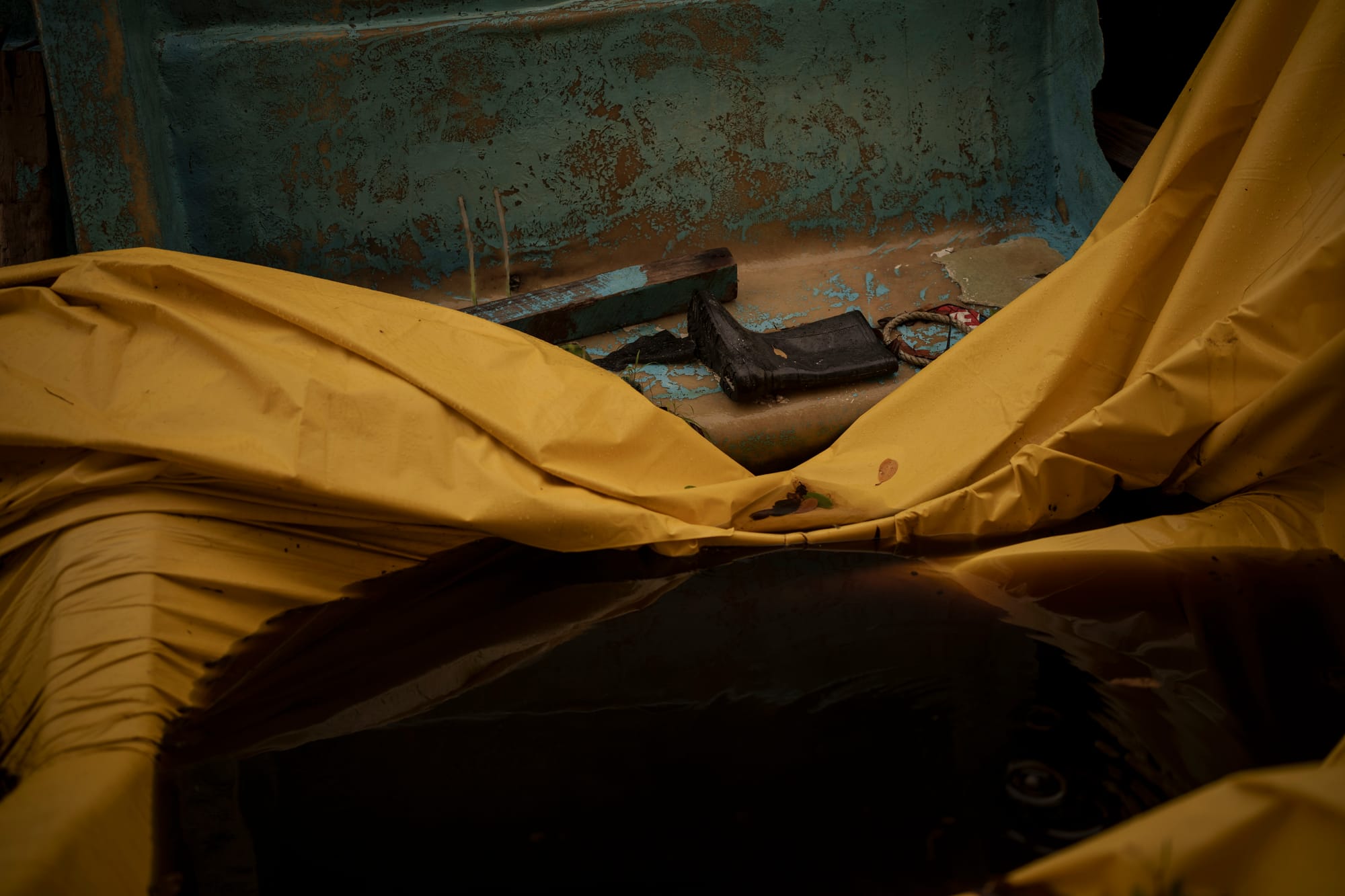 The interior of the boat, containing a single boot, a rope, and a tarp covered in brown water.