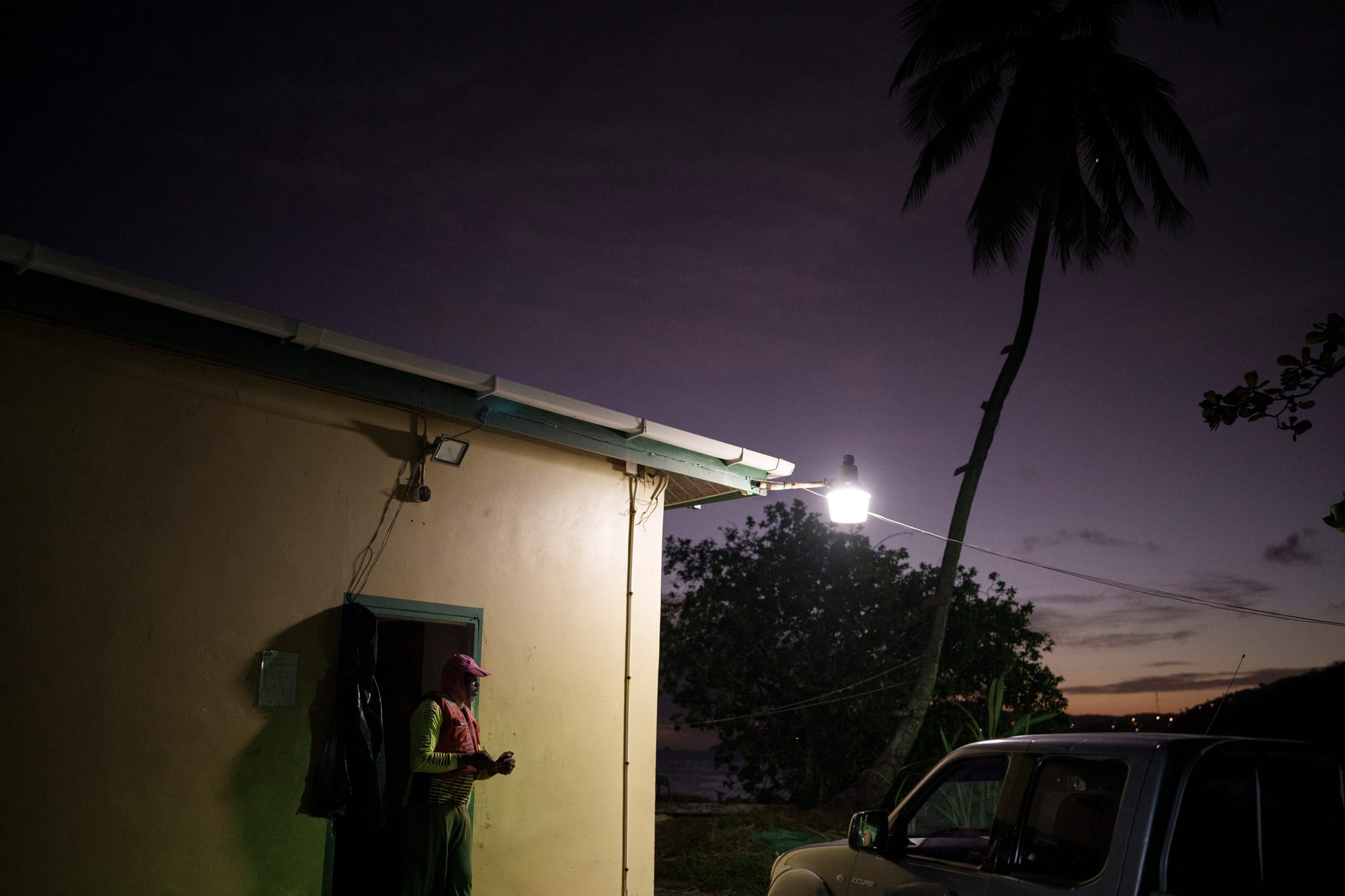 A man in a hat and fishing vest steps out of a building at sunrise.